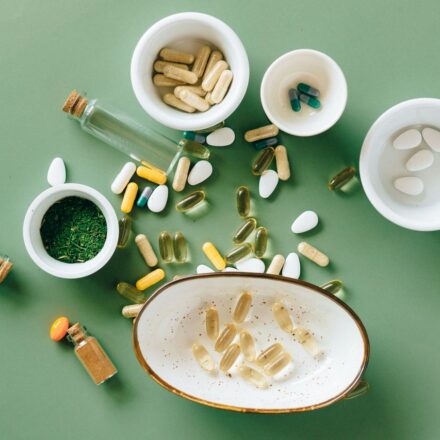 Assorted dietary supplements, capsules, and pills spilling from white bowls on a green surface with herbal powder